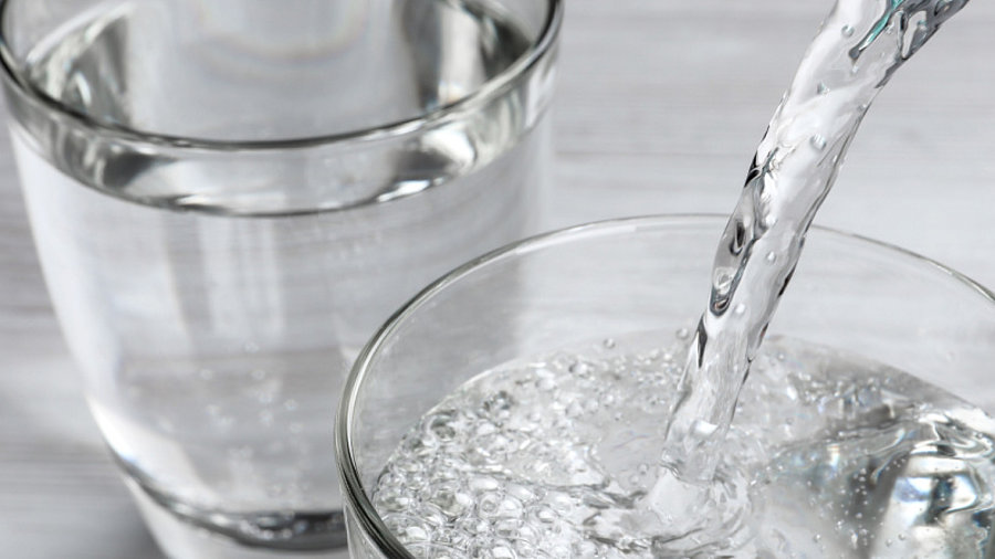 Trinkwasser aus der Flasche in Glas auf wei&szlig;em Holztisch