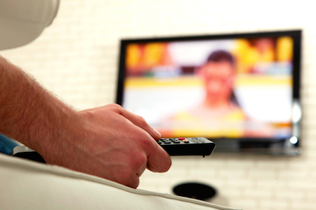 Hand mit Fernbedienung im Vordergrund, Fernseher im Hintergrund