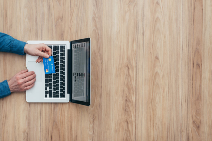 Mann sitzt an Tisch mit Laptop und zahlt online 