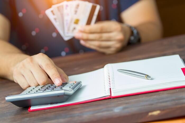 Mann mit Kreditkarten in der Hand bedient Taschenrechner